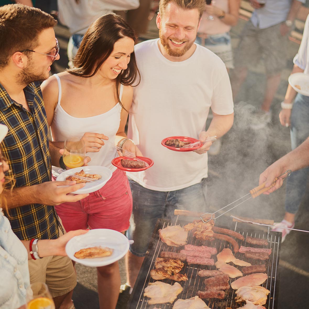 Group of people standing around grill, chatting, drinking and ea ludzie bawiący sie na imprezie
